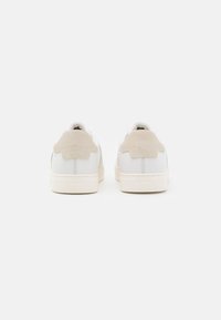 Sneaker bianche in pelle con accentuazione in suede beige sul tallone, punta tonda, suola piatta crema e branding minimo sul retro.