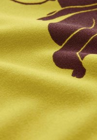 Żółta tkanina o gładkiej, lekko fakturowanej powierzchni z brązowym wzorem kwiatowym; wzór posiada zakrzywione linie i organiczne kształty.