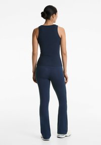 Navy gerippter Tanktop, kombiniert mit eng anliegenden, navyfarbenen Schlaghosen. Das Outfit hat eine glatte Textur und ein einfaches Design.