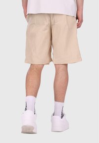 Shorts beiges légers avec une texture à carreaux et des poches latérales, portés avec des baskets blanches et des chaussettes arborant des inscriptions noires.