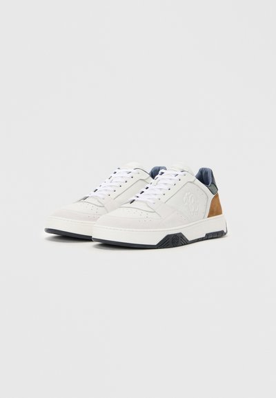 Vita och beige sneakers med en texturerad läderöverdel, snörningsdesign och gummisula. Har en subtil logotyp på sidan och marinblå detaljer.