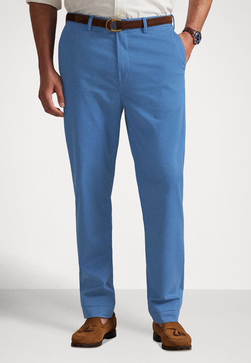 Calças de algodão azul claro com corte reto, fecho plano e dois bolsos laterais. Combinadas com cinto de couro castanho e mocassins.