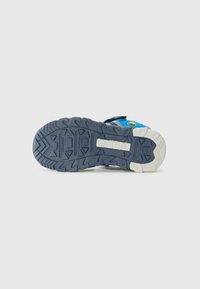 Tălpic de pantof sportiv albastru, cu un model de bandă de rulare robust; material din cauciuc cu un margine de un gri deschis și un grip texturat. Logo-ul brandului este prezent.