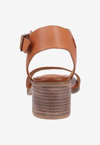 Sandalias de tacón de cuero marrón con una amplia correa en el tobillo, un detalle de hebilla cuadrada y un tacón bloque de color marrón claro con textura.