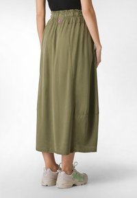 Fustă de culoare verde oliv, până la genunchi, cu talie elastică răsfrântă, dotată cu buzunare laterale și o textură netedă. Purtați cu adidași de culoare deschisă.