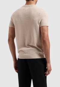 Short-sleeve, light beige knit sweater with a textured finish, round neckline, and ribbed hem. Features a relaxed fit and casual design.