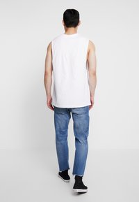 Vit ärmlös skjorta i kombination med ljusblå jeans och svarta ankelskors. Skjortan har rund hals; jeansen har en blekt struktur.