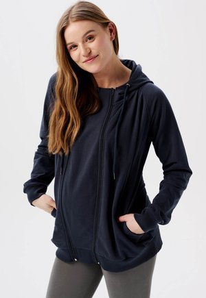Hoodie zippé marine avec capuche, poches, poignets côtelés et ourlet. Tissu doux avec une coupe décontractée, adapté pour un usage quotidien.