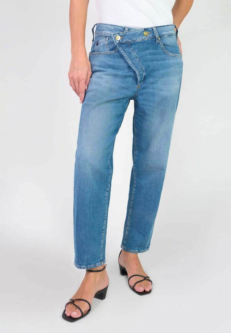 Jean en denim bleu clair avec une coupe décontractée, présentant un design de taille asymétrique unique et deux boutons dorés à l'avant.