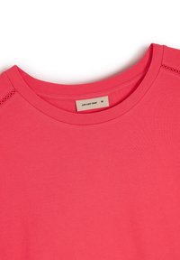 Różowa koszulka z krótkim rękawem, z prążkowanym okrągłym dekoltem i perforowanymi detalami na ramionach. Miękka tekstura materiału. Rozmiar oznaczony jako M.