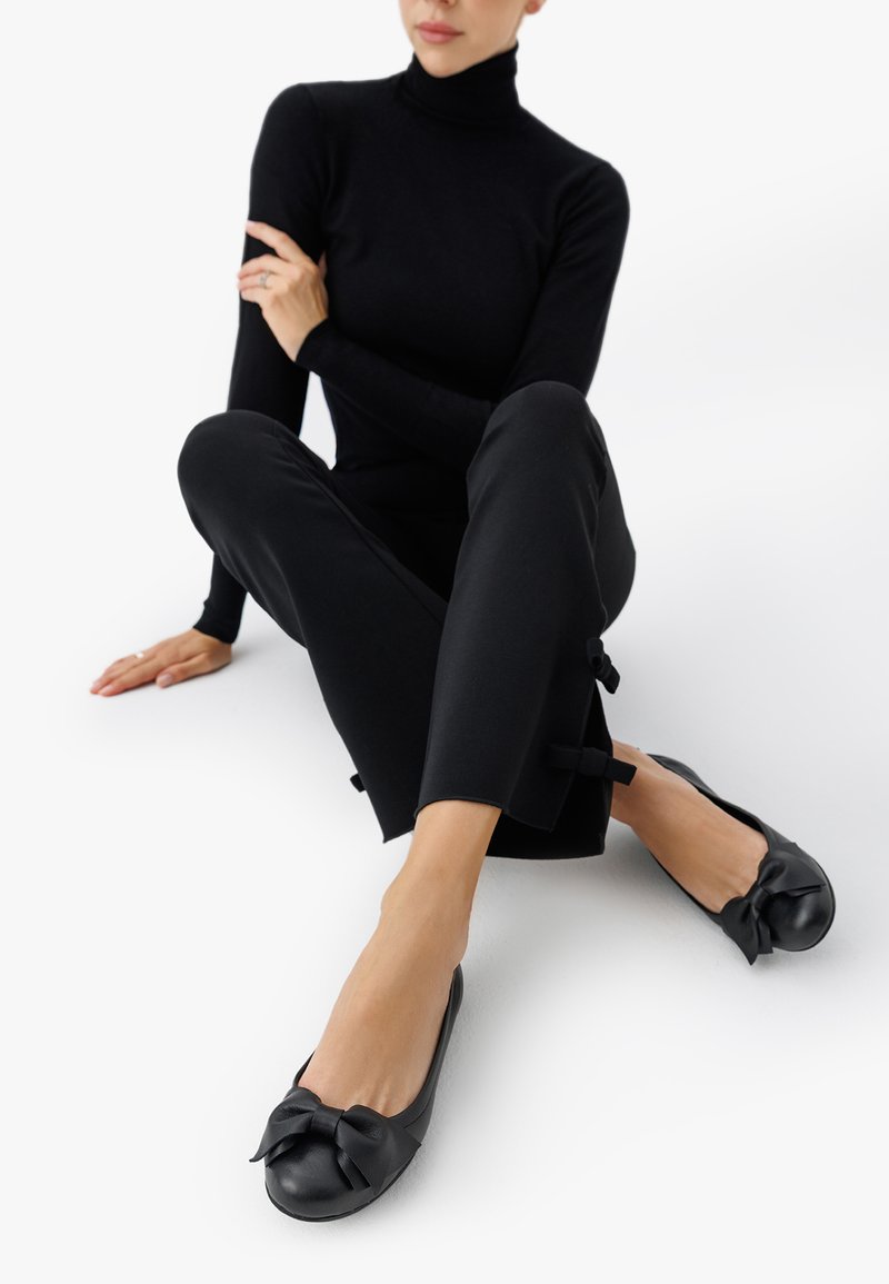 Mustad mustad ballet kingad, millel on nahk ja kaunistuseks vibu varvaste juures, kantud sobivate mustade pükstega, millel on vibu detailid hemimaal.