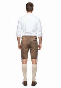 Bruine leren shorts met zijzakken, vetersluitingdetails aan de zoom, gecombineerd met knielange gebreide sokken en bruine schoenen. Witte shirt zichtbaar.