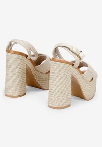 Beige platform heels with a braided rope texture on a chunky heel. Features an ankle strap and open toe design. Smooth leather insole.