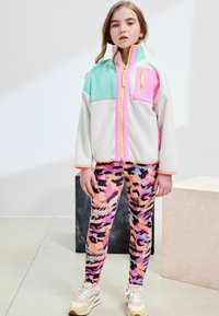 Veste en polaire zippée colorée avec des sections menthe, rose et blanche. Associée à des leggings à motifs dans des tons rose, violet et noir.