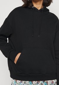 Svart hoodie med justerbara dragsnören, känguruficka, ribbade muddar och fåll. Mjukt tyg, avslappnad passform, minimalistisk design.