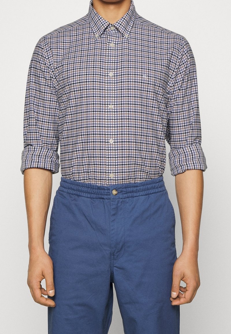 Rutigt skjorta i blått, vitt och brunt; knäppdesign med spridd krage och uppvikta ärmar. Matchat med blåa byxor med elastisk midja.