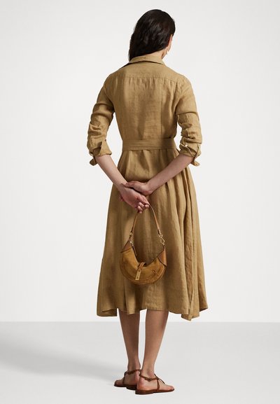 Robe en lin beige à manches longues et taille ceinturée, assortie à un petit sac à main beige et des sandales marron. Corsage ajusté et jupe évasée.