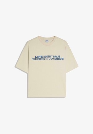 Bež kratka majica s kratkim rukavima s plavim tekstom "LIFE DOESN'T BRAKE FOR DOUBTS 2026" i dva mala logotipa preko prsiju.