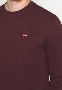 Långärmad maroon t-shirt i bomull med en liten röd Levi's-logotyp på bröstet, med en klassisk rund halsringning och slät textur.