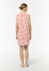 Ärmelloses, knielanges Kleid mit pink- und orangefarbenem abstraktem Muster. Glattes Material mit einem Reißverschluss im Rücken. Flache Sandalen sind sichtbar.