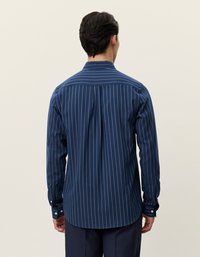 Sötétkék csíkos ing, texturált anyagból készült. Gombos gallérral, hosszú ujjakkal és ívelt alsó széllel rendelkezik.