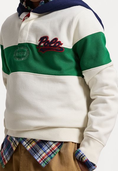 Pullover em creme e verde, com capuz azul. Apresenta um logótipo bordado "Polo". Usado sobre uma camisa xadrez com detalhes em verde e azul.