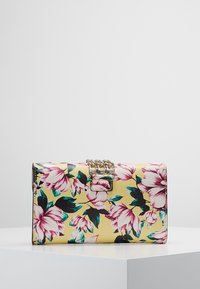 Blomstermønstret pung med en gul imiteret læderoverflade udsmykket med pink og teal blomster, en sølvkæde accent og en låselse.