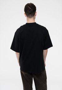 Black cotton t-shirt with a relaxed fit, short sleeves, and a crew neckline, worn with dark brown corduroy pants.