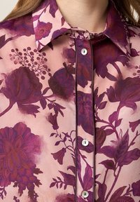 Silk blouse in light pink with large dark purple floral patterns. Features a pointed collar, button placket, and subtle sheen.