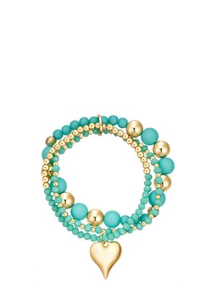 Bracelet superposé avec des perles turquoises et dorées alternées, présentant un charm en forme de cœur lisse en or suspendu à un brin.