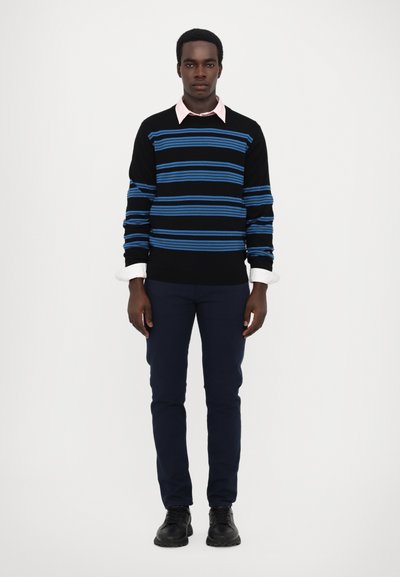 Pull noir avec des rayures horizontales bleues sur une chemise col rose pâle; associé à un pantalon marine et des chaussures noires. Texture lisse.