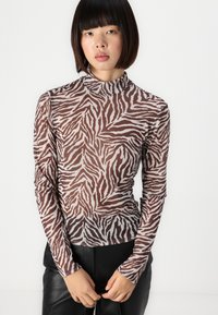 Dugih rukava majica od prozirne smeđe tkanine s bijelim zebra prugama, s visokim ovratnikom i prilagođenim dizajnom. Uparen s crnim kožnim hlačama.