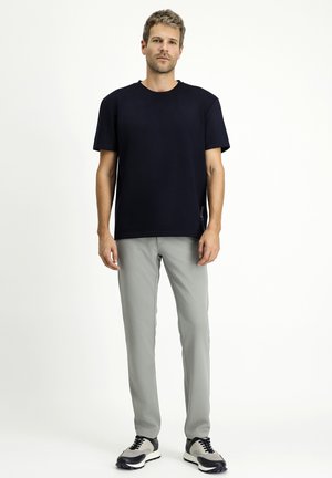 Camiseta de algodón azul marino, de manga corta y cuello de tripulación. Combinada con pantalones ajustados de color gris claro y zapatillas en blanco y negro. Diseño sencillo, sin estampados.