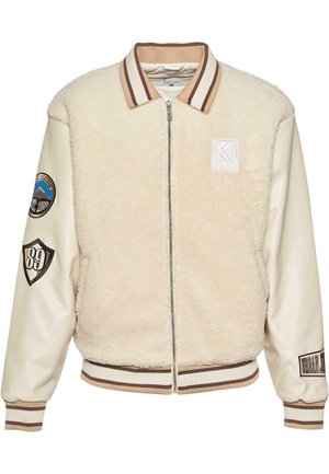 Krämfärgad bomberjacka med ett shearling-ärme, släta lädersleeves, ribbad krage och ärmslut, samt broderade lappar på ärmarna.
