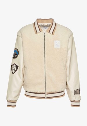 Cremefarbene Bomberjacke mit einem Shearling-Körper, glatten Lederärmeln, geripptem Kragen und Bündchen sowie gestickten Patches an den Ärmeln.