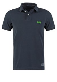Polo bleu marine à manches courtes avec deux boutons, logo vert brodé sur la poitrine gauche et une petite étiquette près de l'ourlet.