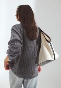Pull en tricot gris à mailles avec une coupe décontractée ; sac fourre-tout structuré de couleur claire avec des accents noirs ; modèle de dos, look décontracté.