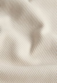 Tissu côtelé de couleur crème avec des plis doux et des lignes verticales texturées créant un motif ondulé.