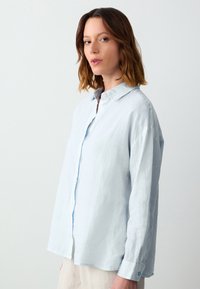 Himmelblaues Leinenhemd mit Knopfleiste, Kragen und langen Ärmeln. Strukturiert Stoff mit lockerer Passform und Seitenschlitzen am Saum.