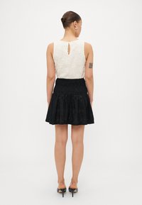Top branco de renda floral com costas em forma de buraco de chave, combinado com uma saia preta de eyelet. A saia tem detalhes franzidos e alarga na parte inferior. Sapatos de salto pretos.