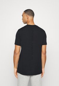 Černé tričko s krátkým rukávem s texturovaným vzorem, s vertikálním logem "UNDER ARMOUR" v matném provedení na zadní straně.