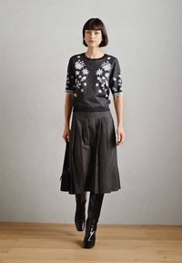 Πλεκτό μαύρο πουλόβερ με λευκά λουλουδάτα μοτίβα, συνδυασμένο με πλισέ γκρίζα φούστα και λαμπερά μαύρα μπότες μέχρι το γόνατο. Λείος υφασμάτινος χαρακτήρας, κομψός σχεδιασμός.