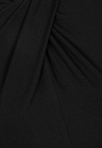 Czarna tkanina o gładkiej fakturze z marszczonymi sekcjami, tworzącymi efekt drapowania. Szczegóły szwów są widoczne w pobliżu linii zagięć.