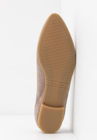 Suela de zapato de ante color marrón claro con una base de goma, presentando un patrón texturizado y un logotipo grabado. El tacón es bajo y redondeado para mayor comodidad.