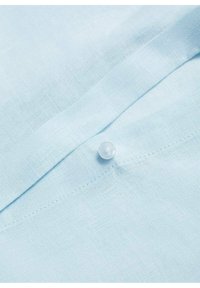 Tissu bleu clair avec une couture fine, présentant un seul petit bouton rond blanc cousu sur le tissu.