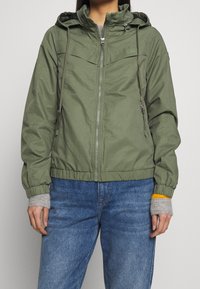 Olivengrøn hættejakke i letvægtsmateriale med lynlås foran, elastiske manchetter og kant; har to sidelommer og et enkelt design.