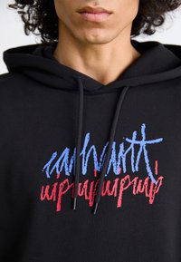Felpa nera con un design di testo astratto in blu e rosso. Presenta corde di regolazione e una texture soffice adatta per l'abbigliamento casual.