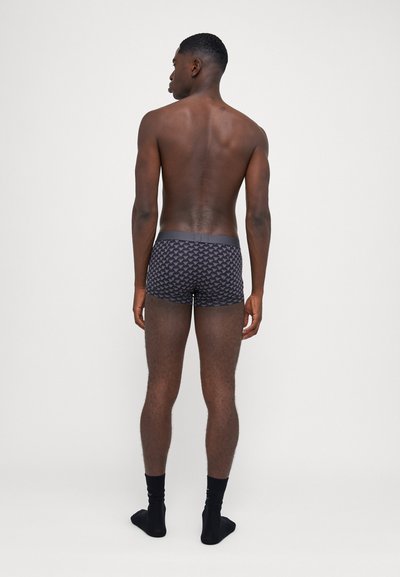 Boxers noirs avec un design à motifs, taille élastique et tissu lisse. Modèle présenté de dos, portant des chaussettes noires à la cheville.