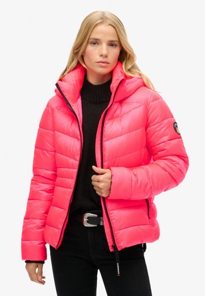 Doudoune rose vif avec capuche, design matelassé et fermeture éclair noire. Portée sur un pull en tricot noir ; présente un logo sur la manche.