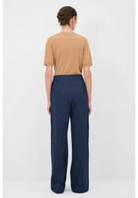 Hnědý top s krátkým rukávem v kombinaci s námořnickými kalhotami s širokými nohavicemi. Top má jednoduchý design, zatímco kalhoty mají hladkou texturu a vysoký pas.